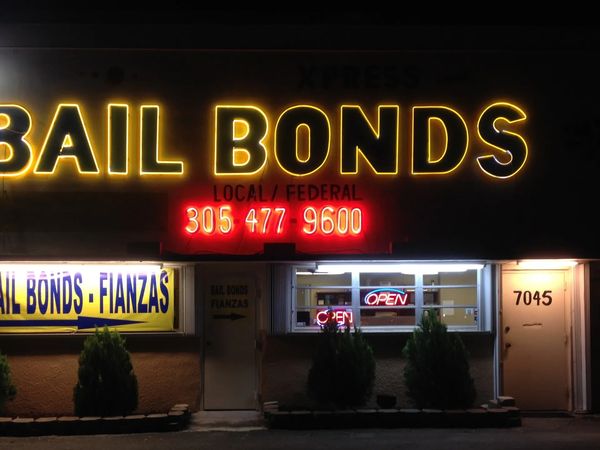 Xpress Bail Bonds storefront at night — glowing neon BAIL BONDS sign, 305-477-9600, Bail Bonds · Fianzas, OPEN